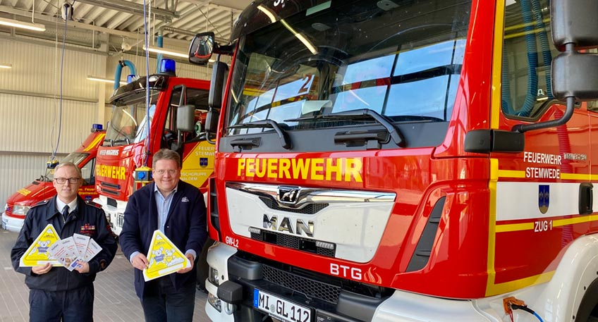 Stemwede ein St&uuml;ck sicherer machen: B&uuml;rgermeister Kai Abruszat (re.) und Gemeinde-Kinderfeuerwehrwart Torsten Fischer mit den (f&uuml;r das Foto vergr&ouml;&szlig;erten) Kinderfinder-Aufklebern.