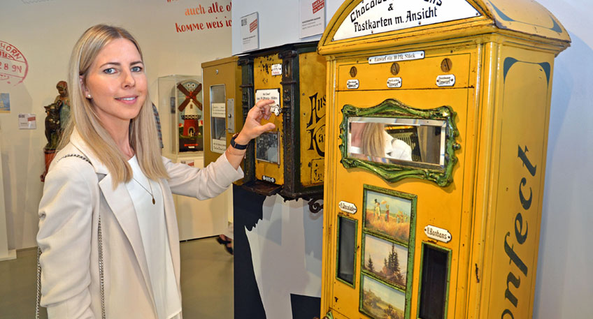 Automatengeschichte zum Anfassen: Annika Maucher an einem Münzautomaten, der Schokolade, Bonbons und Ansichtskarten zur Verfügung stellt.