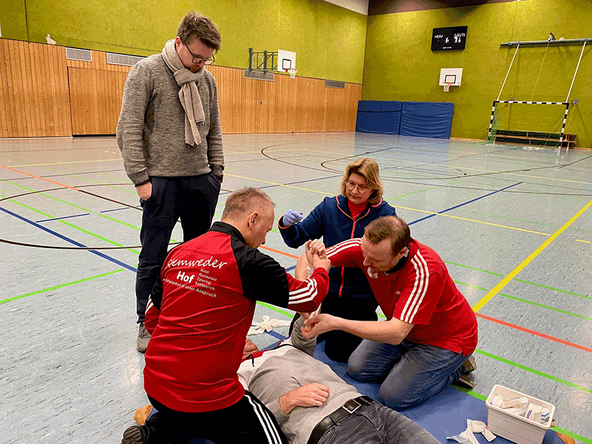Ralf Freese (li.) und Christian Brinkmeier legen gemeinsam einen Druckverband an. Susanne Altvater vom DRK und Christian B&auml;cker (stehend) schauen &uuml;ber die Schulter und geben Tipps.