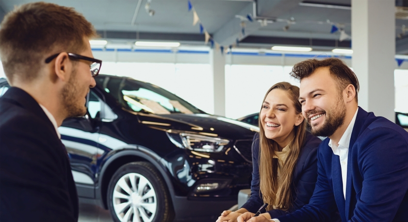 Junge Frau und junger Mann sitzen im Autohaus und verhandeln einen Autokauf