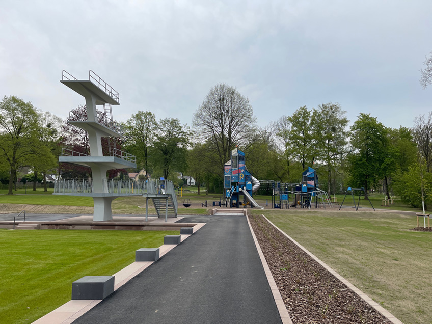 Das hier mal ein Freibad war lässt sich noch gut erkennen. Die Architektur folgt der alten Struktur. So wurde ein Wiesenstück geschaffen, das innerhalb des alten Schwimmerbeckens angelegt wurde. Die ehemaligen Sprungtürme sind nun Sitzgelegenheiten, auf die Fläche führt eine Treppe in ähnlicher Weise, wie zu Freibadzeiten. Auch der Sprungturm wurde erhalten und dient nun als Aussichtsturm.   Die Spielplätze wurden für unterschiedliche Altersstufen entworfen und suchen ihresgleichen. Ein so großes Angebot findet sich kaum in der Region. Hier kann man gut und gerne einen Tag verbringen, nicht nur einige Stunden. Große Wiesenflächen und Sitzgelegeheiten laden zum Verweilen oder Spielen ein, und das alles barrierefrei. Ein Kneippbecken und Outdoor-Fitnessgeräte runden das Freizeitangebot ab. Dieser Park ist ein echtes Highlight für die Lübbecker und wird sicher nicht nur Familien schöne Zeiten ermöglichen.   Quelle: Stadt Lübbecke, Fotos: Hallo Lübbecke