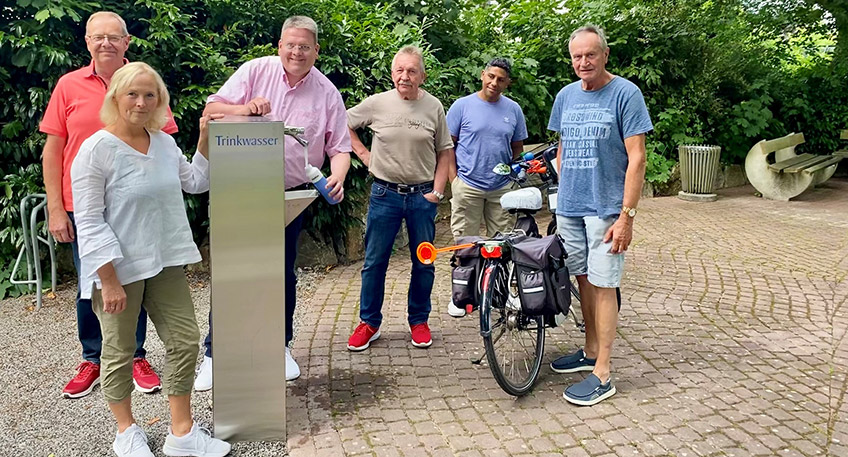 Frisches Trinkwasser auf Knopfdruck: Daniela Niermann (2.v.li.) und Ralf Tacke (li.) vom Verein Leben in Wehdem zusammen mit B&uuml;rgermeister Kai Abruszat (3.v.li.). G&uuml;nter Kr&ouml;ger (3.v.re.) und Gerd Bick (re.) von der ZWAR-Fahrradgruppe sowie Andr&eacute; Cardoso M&uuml;hlig aus M&uuml;nster begutachten die neue Zapfanlage. 